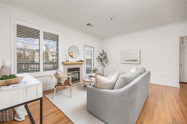 living area with crown molding, a tile fireplace, light wood-style floors, and baseboards