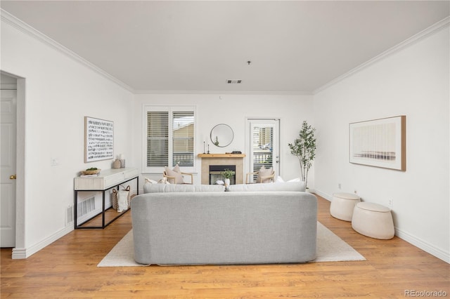 living room with crown molding, a fireplace, light wood finished floors, and baseboards
