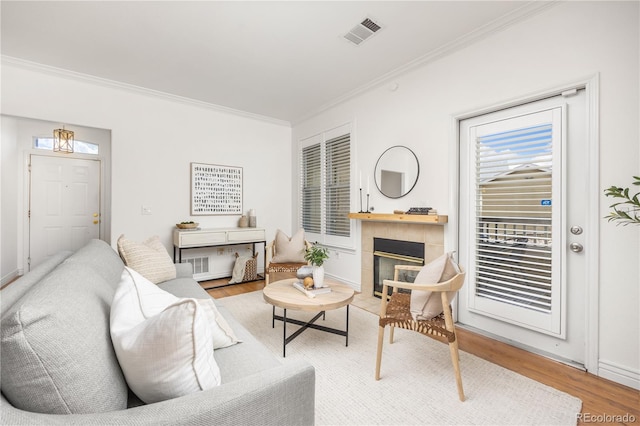 living area featuring crown molding, wood finished floors, a tiled fireplace, and baseboards