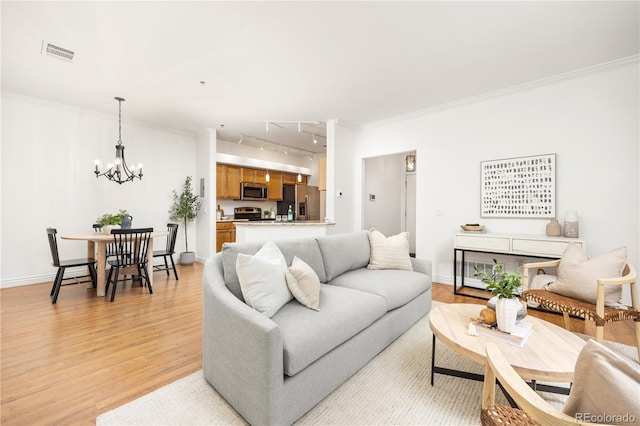 living room with rail lighting, light wood-type flooring, a chandelier, ornamental molding, and baseboards
