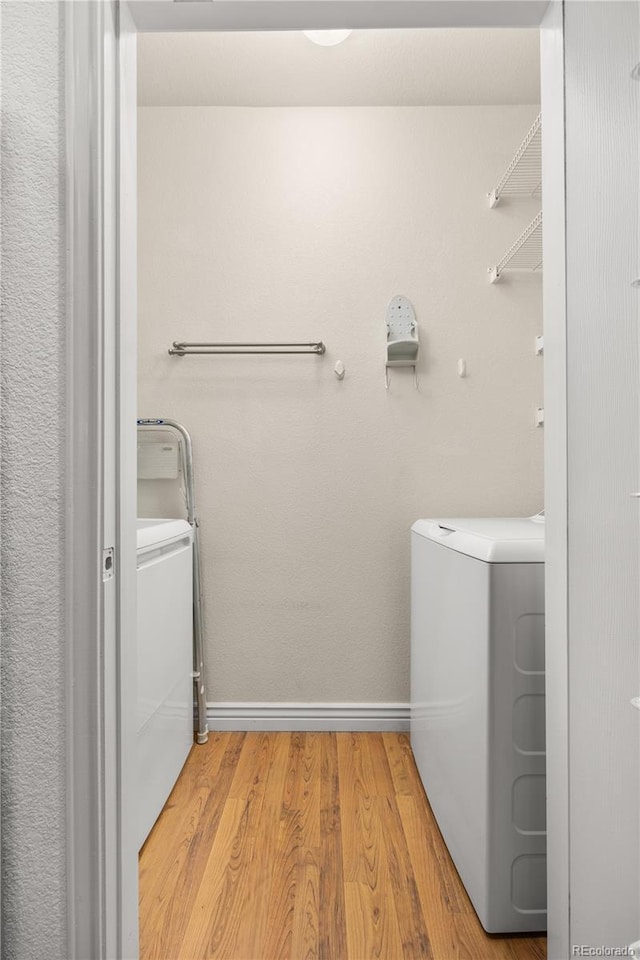 laundry area with washing machine and dryer, light wood-type flooring, and baseboards