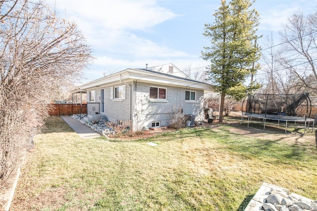 rear view of house with central air condition unit, fence, brick siding, a trampoline, and a lawn