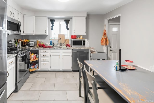 kitchen featuring stainless steel appliances, a sink, light tile patterned flooring, light stone countertops, and white cabinetry