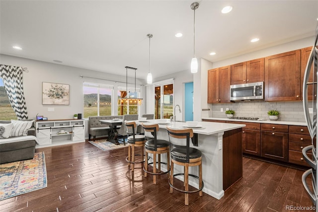 kitchen featuring light countertops, stainless steel microwave, dark wood-type flooring, tasteful backsplash, and a breakfast bar area