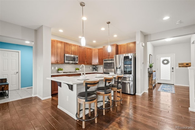 kitchen featuring a kitchen breakfast bar, tasteful backsplash, stainless steel appliances, light countertops, and dark wood finished floors