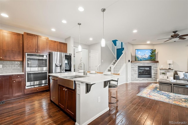 kitchen with a sink, open floor plan, light countertops, dark wood-type flooring, and appliances with stainless steel finishes