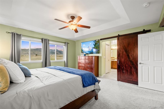 bedroom with ensuite bath, a barn door, light carpet, and ceiling fan