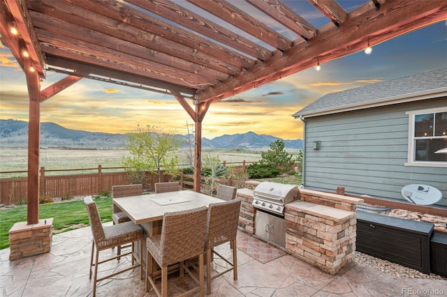 patio terrace at dusk featuring a pergola, area for grilling, fence, and a mountain view