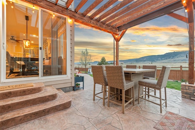 patio terrace at dusk featuring fence, outdoor dry bar, and a mountain view