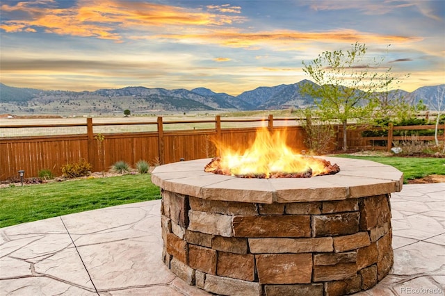 patio terrace at dusk with a yard, fence, an outdoor fire pit, and a mountain view