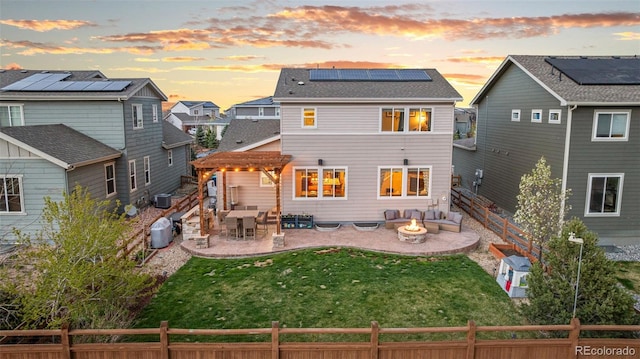 back of property at dusk featuring a fenced backyard, an outdoor fire pit, and solar panels