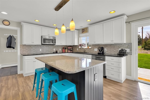 kitchen with stainless steel appliances, baseboard heating, a sink, light wood finished floors, and recessed lighting