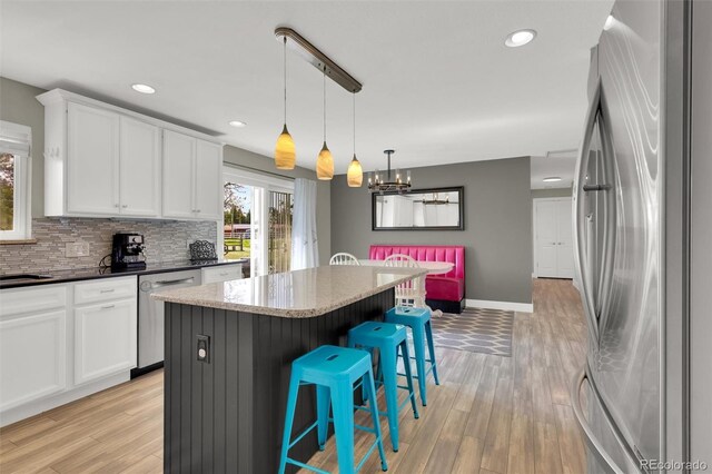 kitchen with stainless steel appliances, a center island, backsplash, a kitchen bar, and white cabinets