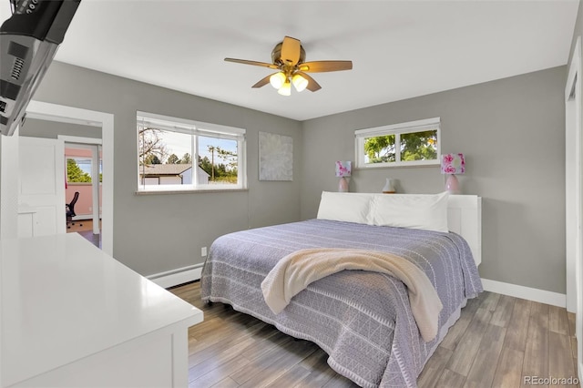bedroom with a baseboard radiator, baseboards, wood finished floors, and a ceiling fan