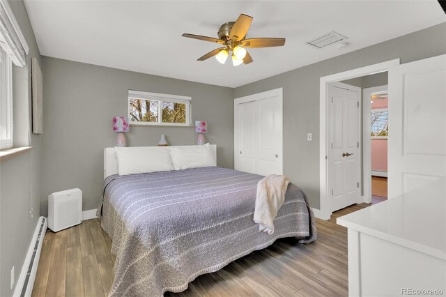 bedroom featuring baseboard heating, wood finished floors, baseboards, and a closet
