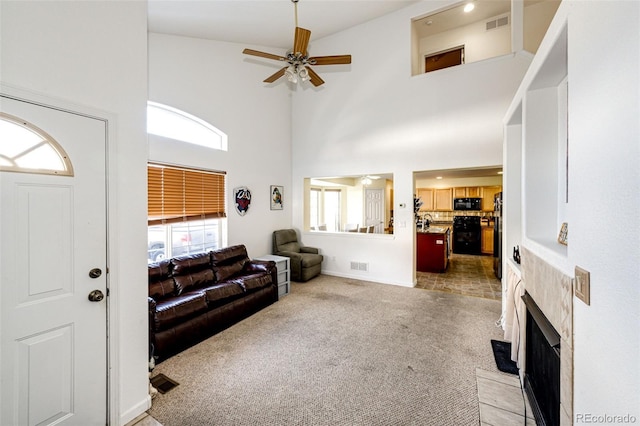 carpeted living room with a fireplace, a towering ceiling, and ceiling fan