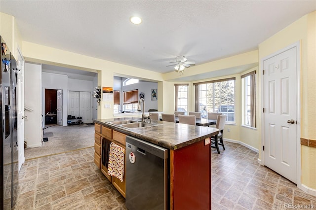 kitchen featuring stainless steel dishwasher, light colored carpet, ceiling fan, a kitchen island with sink, and sink