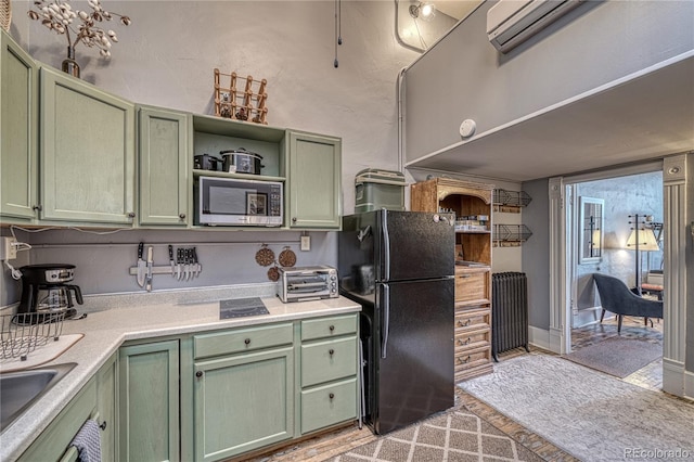 kitchen featuring radiator heating unit, stainless steel microwave, black fridge, and green cabinetry