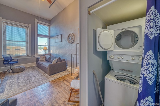 clothes washing area with laundry area, stacked washer and dryer, a ceiling fan, wood finished floors, and baseboards