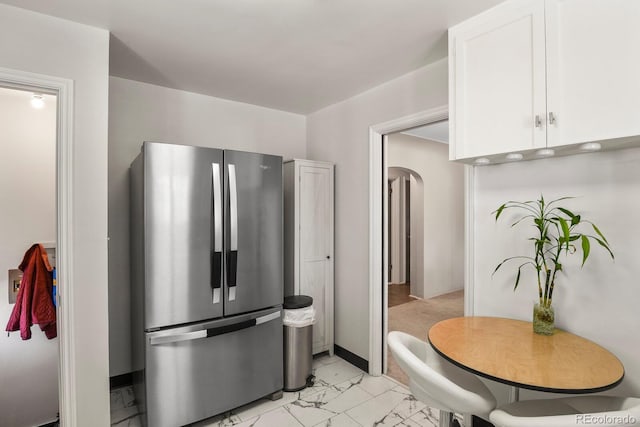 4546 S Logan St, Englewood, CO 80113 - kitchen with freestanding refrigerator, white cabinetry, light marble finish floors, arched walkways, and baseboards