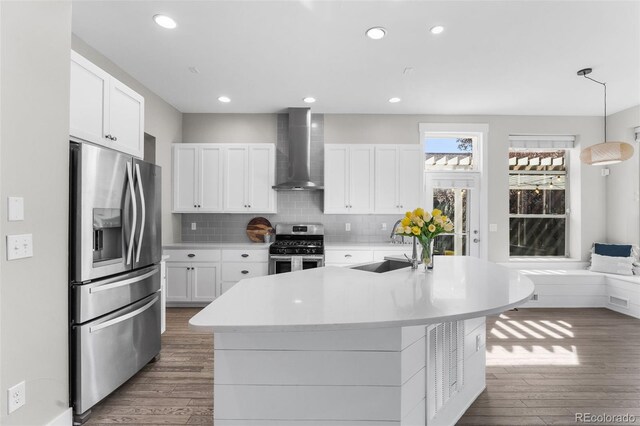 kitchen with pendant lighting, white cabinets, stainless steel appliances, and wall chimney range hood