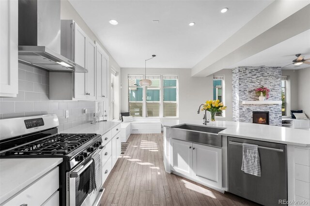 kitchen with wall chimney exhaust hood, stainless steel appliances, sink, pendant lighting, and white cabinets