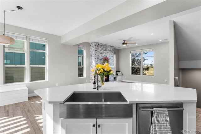 kitchen featuring sink, hanging light fixtures, stainless steel dishwasher, ceiling fan, and light wood-type flooring