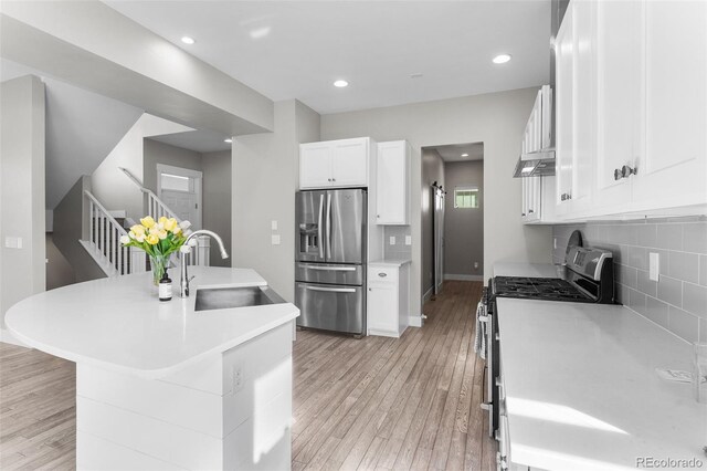 kitchen featuring sink, backsplash, appliances with stainless steel finishes, white cabinets, and light wood-type flooring