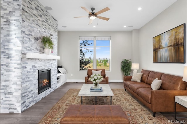 living room featuring dark hardwood / wood-style flooring, a stone fireplace, and ceiling fan