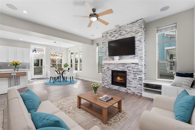 living room featuring a tiled fireplace, light hardwood / wood-style flooring, and ceiling fan with notable chandelier