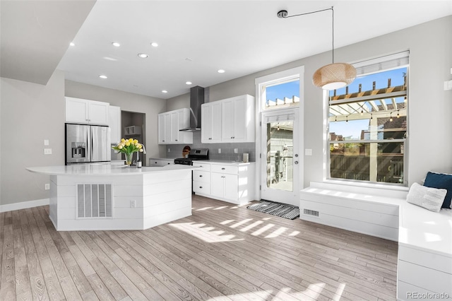 kitchen featuring wall chimney exhaust hood, stainless steel appliances, pendant lighting, light hardwood / wood-style floors, and white cabinets