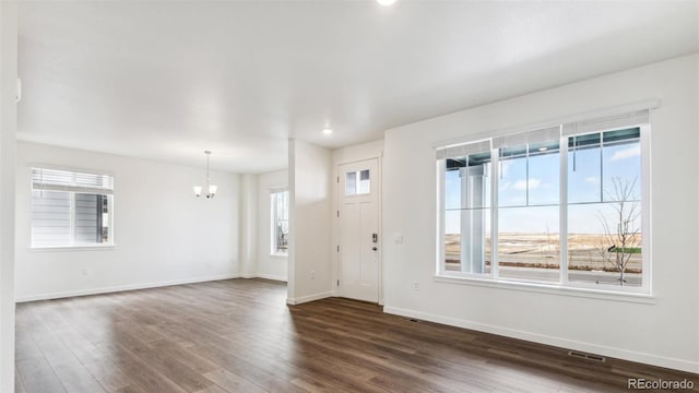 unfurnished living room featuring dark hardwood / wood-style floors, plenty of natural light, and a notable chandelier