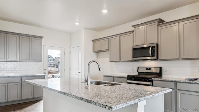 kitchen featuring light stone countertops, stainless steel appliances, a center island with sink, and sink