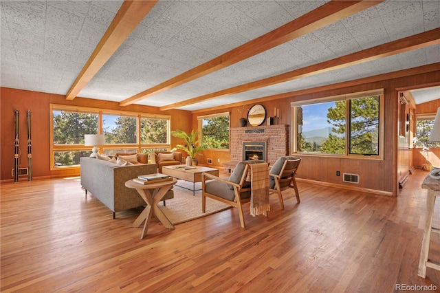 living room featuring wood walls, a healthy amount of sunlight, light wood-type flooring, and beam ceiling