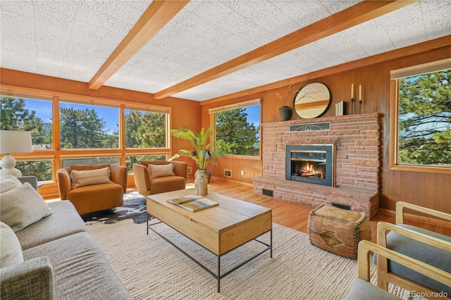 living room featuring a brick fireplace, a wealth of natural light, beamed ceiling, and light wood-type flooring