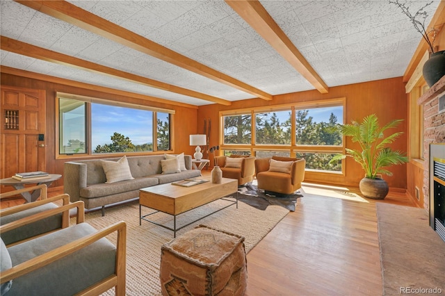 living room with beam ceiling, a wealth of natural light, wooden walls, and light wood-type flooring