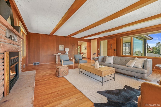 living room with beamed ceiling, wood walls, wood-type flooring, and a textured ceiling