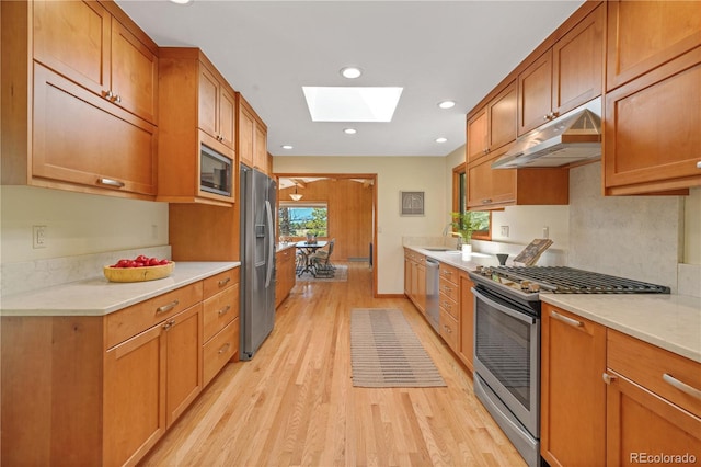 kitchen with appliances with stainless steel finishes, a skylight, light hardwood / wood-style floors, and sink