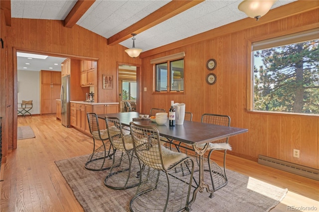 dining area featuring vaulted ceiling with beams, wood walls, a healthy amount of sunlight, and light hardwood / wood-style floors