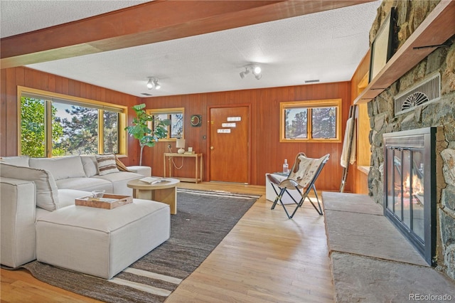 living room featuring a fireplace, a textured ceiling, hardwood / wood-style flooring, and wooden walls