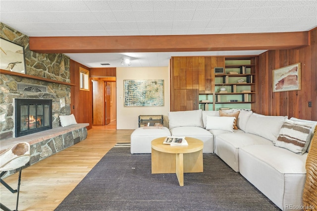 living room with beamed ceiling, hardwood / wood-style flooring, a stone fireplace, and wood walls