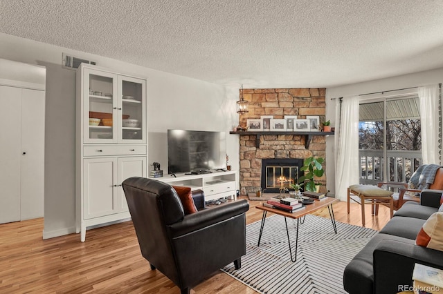 living room featuring a textured ceiling, a stone fireplace, light wood finished floors, and visible vents