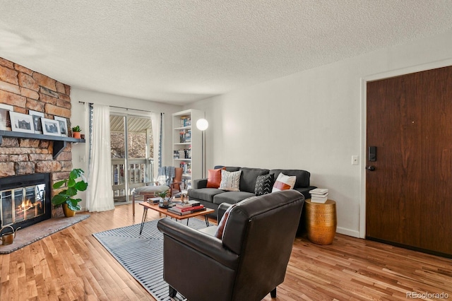 living area with a textured ceiling, a stone fireplace, and wood finished floors