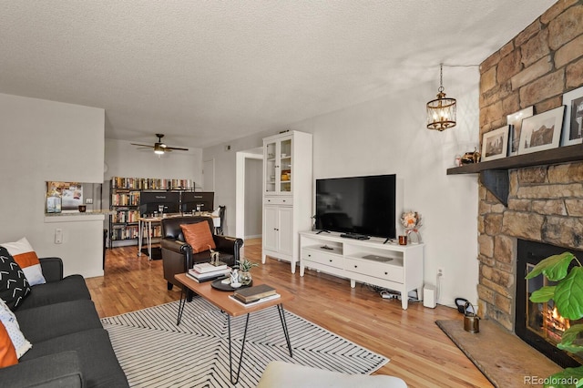 living room featuring a textured ceiling, a fireplace, a ceiling fan, and wood finished floors