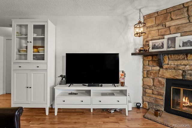 living area with a textured ceiling, an inviting chandelier, a stone fireplace, and wood finished floors