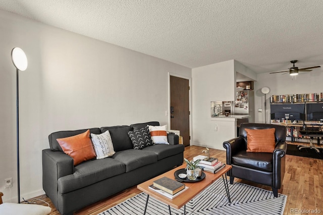 living room with light wood-type flooring, a ceiling fan, and a textured ceiling