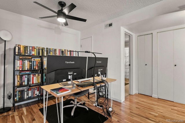 home office with a textured ceiling, a ceiling fan, wood finished floors, and visible vents