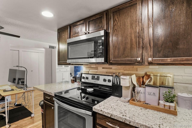 kitchen with dark brown cabinets, appliances with stainless steel finishes, light stone counters, light wood-style flooring, and visible vents