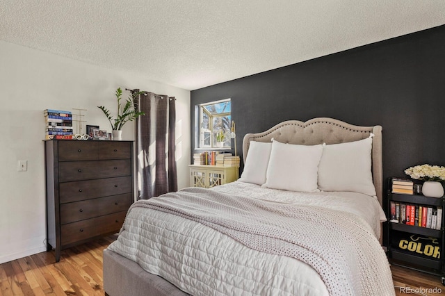 bedroom with baseboards, a textured ceiling, and wood finished floors