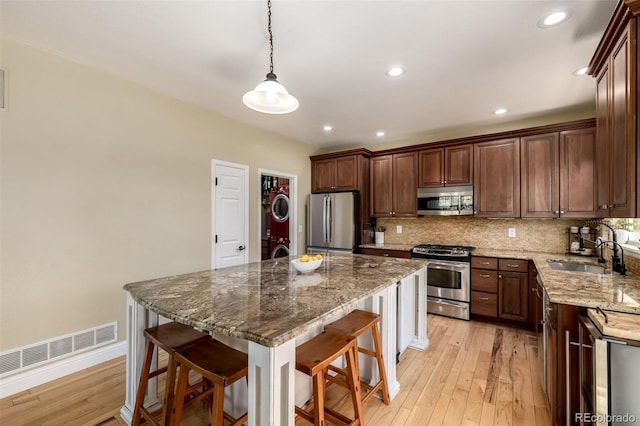 902 Jarvis Dr, Erie, CO 80516 - kitchen with stainless steel appliances, a sink, stacked washer and clothes dryer, a kitchen bar, and decorative backsplash